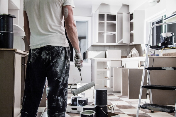 A man with paint smears on his clothes stands ready to paint a bare kitchen.