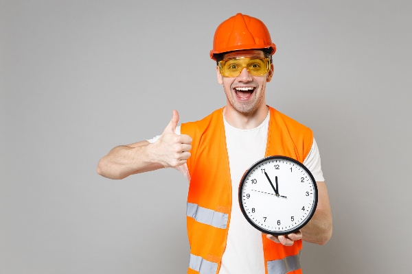 A construction worker holds a clock and gives the camera a thumbs up.